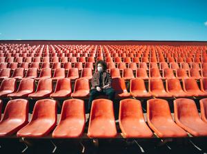 Coronavirus protection, woman in medical mask sitting with smartphone on a bench in empty city stadium.