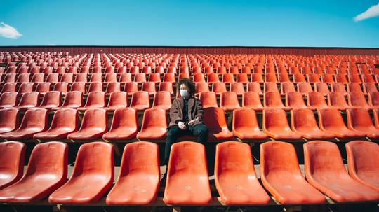 Coronavirus protection, woman in medical mask sitting with smartphone on a bench in empty city stadium.