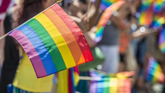 Close-Up Of Rainbow Flag With Crowd In Background During Parade