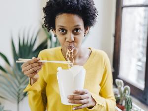 Young woman eating Asian noodles for lunch with chopsticks