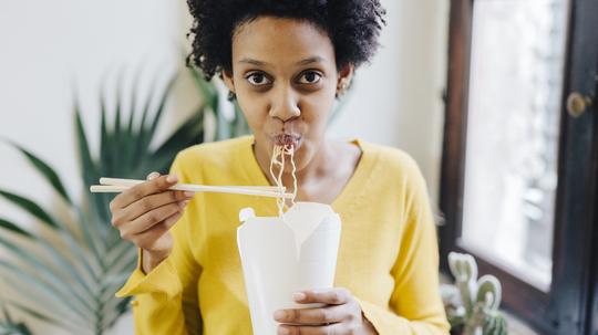 Young woman eating Asian noodles for lunch with chopsticks