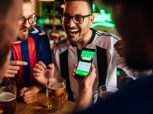 Friends drinking beer, watching soccer game and using mobile app for betting