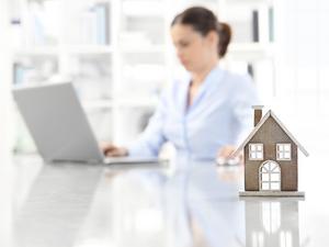 real estate office, home leaning on desk and woman agent working on computer in background