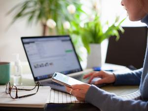 Woman working from home using laptop computer while reading text message on mobile phone