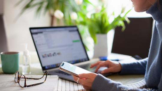 Woman working from home using laptop computer while reading text message on mobile phone