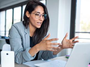 Confident business woman looking and speaking through the webcam while making a video conference with laptop from the office.