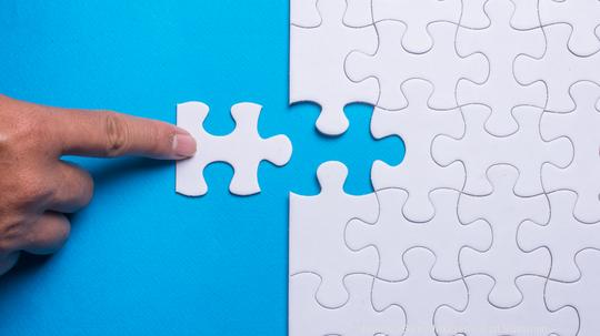 Hand holding piece of white puzzle on blue background. Business and team work concept.