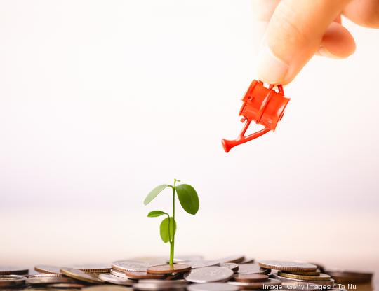 Woman hand holding red watering can with  money stack and seedling on top.