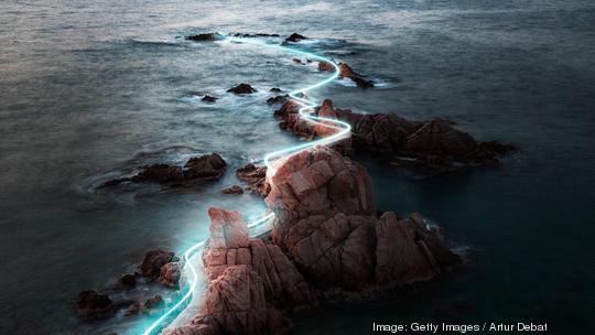 Blue light trail following footpath between the stunning coastline during sunrise.