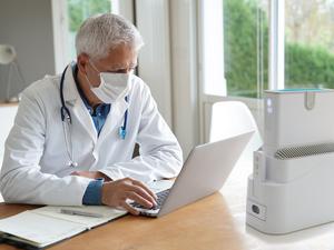 Doctor in office working on laptop, wearing protection mask