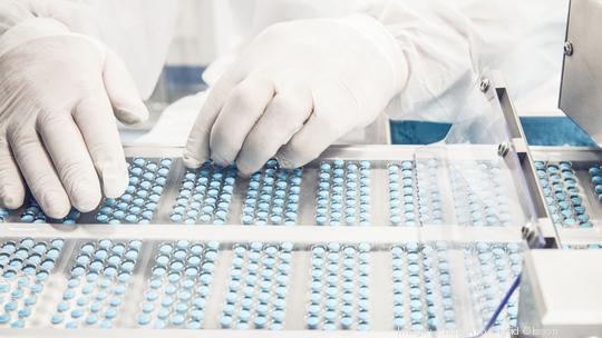 Worker inspecting pills on blisterpack conveyer belt