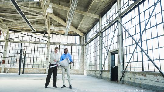 Businessmen reading blueprints in empty warehouse