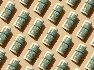 Roll of American dollars banknotes on the beige background, Getty Images