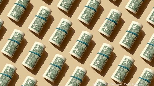 Roll of American dollars banknotes on the beige background, Getty Images