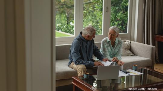 Active senior couple calculating bills in living room - stock