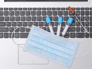 Medical test tubes with syringe and face mask on laptop keyboard. Top view