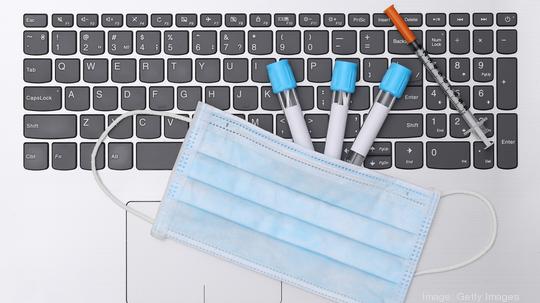 Medical test tubes with syringe and face mask on laptop keyboard. Top view