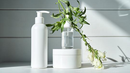 Skin care products on a chest of drawers against a white wooden wall. - stock