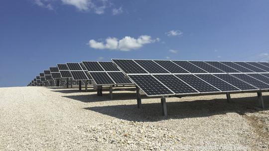 Solar panels on field against blue sky during sunny day