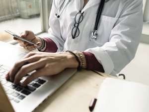 close-up of a female doctor using computer and smartphone