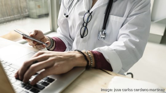 close-up of a female doctor using computer and smartphone