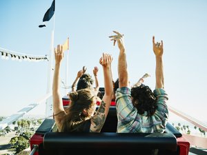 Rear view of couple with arms raised about to begin descent on roller coaster in amusement park