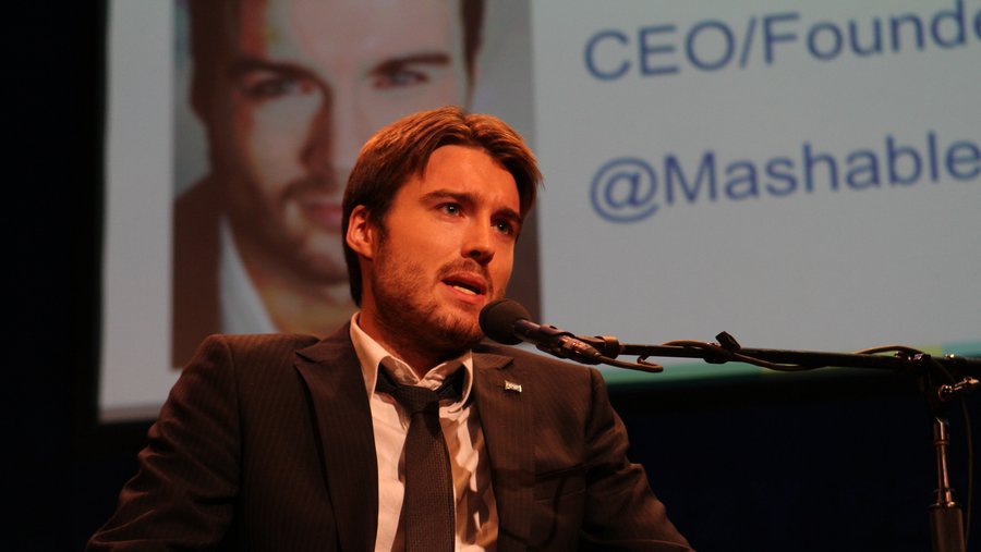 Pete Cashmore speaks at a microphone with CEO and founder and the Mashable handle projected behind him