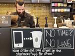 A Starbucks barista partner works behind a Starbucks app sign in Seattle, Washington